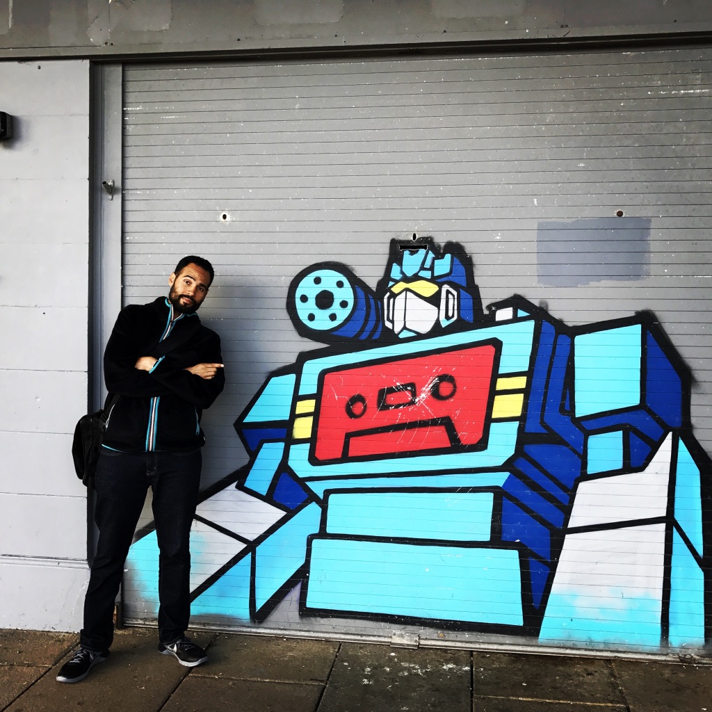Kyle murdock standing in front mural of a transformer with tape deck on its chest plate